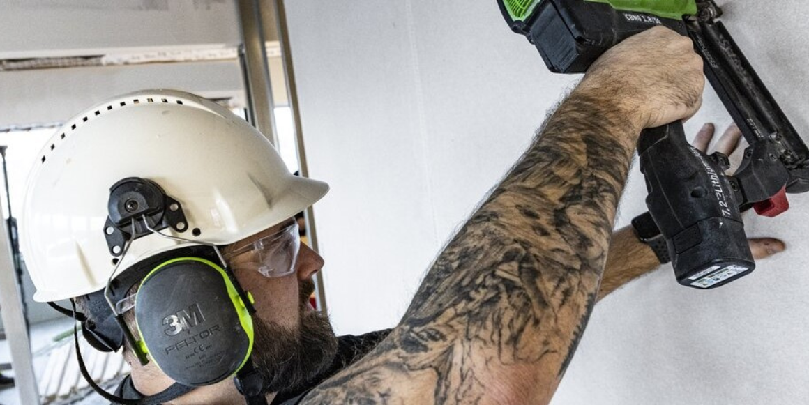En tømrer-mann bruker en drill for å legge gipsplater på veggen.