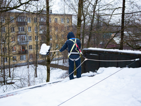 mann som måker snø av tak på hus i et borettslag